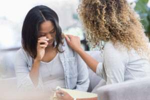 Caring therapist places her hand on a young woman's shoulder as the woman cries during a therapy session.